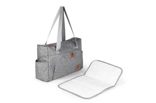 La Bolsa de pañales de maternidad gris de micu micu, con correas largas y múltiples bolsillos, se encuentra junto a un cambiador blanco. Ideal para organizar productos para bebés con entrega gratis en Mallorca, tiene un bolsillo frontal con cremallera y tela texturizada. El cambiador abierto se encuentra a la derecha.