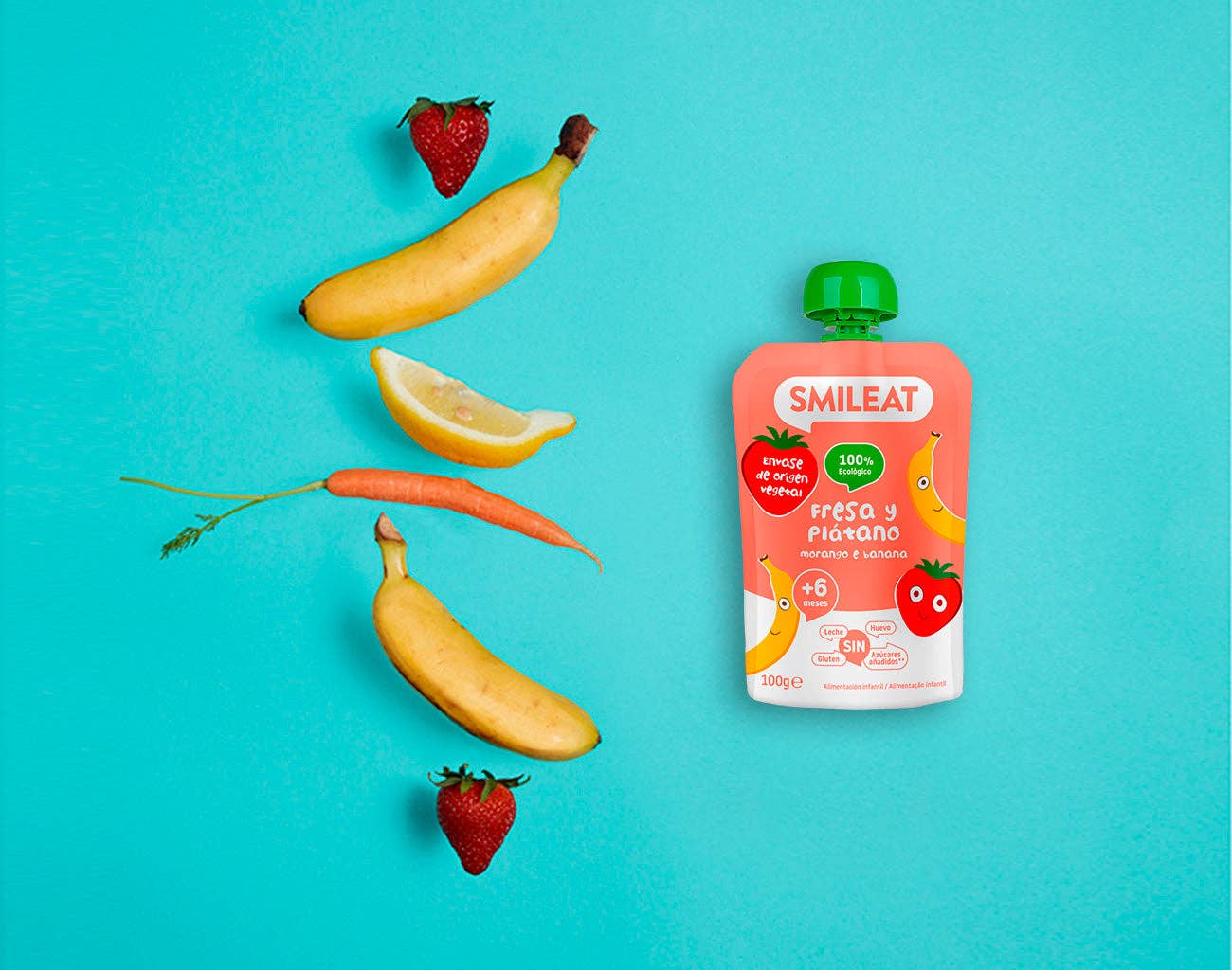 Una foto plana que muestra un Smileat - Pouch Fresa y Plátano Ecológico sobre un fondo azul, rodeado de fresas, plátanos, una rodaja de limón y una zanahoria, ideal para padres  que buscan productos aptos para bebés con opciones de entrega convenientes.