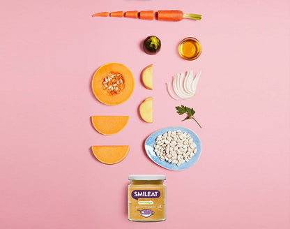 Un diseño de ingredientes frescos sobre un fondo rosa con zanahoria, coles de Bruselas, aceite de oliva, rodajas de cebolla, perejil, judías blancas y rodajas de calabaza rodea un tarro de Smileat Guisito de alubias 230g Ecológico. Explora las ofertas en parafarmacia infantil para ver más opciones deliciosas.