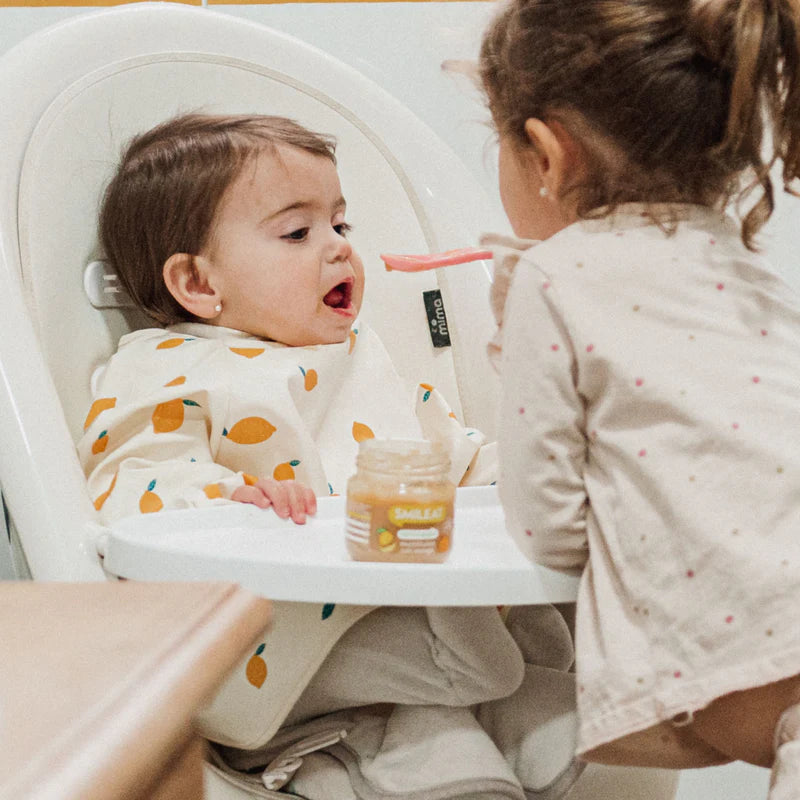 niña dando de comer a hermanita tarrito multifruta 