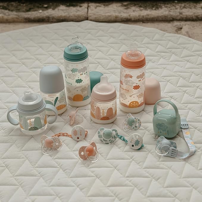 Una colección de artículos para bebés reposa sobre una superficie acolchada, con biberones Suavinex con tapas en tonos pastel, chupetes y pinzas para el pelo en menta, melocotón y crema. Adornado con divertidos diseños de nubes y animales. Aprovecha las ofertas en parafarmacia infantil para completar las necesidades de tu cuarto de bebé.